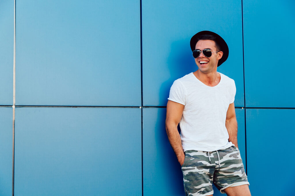 Young man in sunglasses standing on the blue wall background